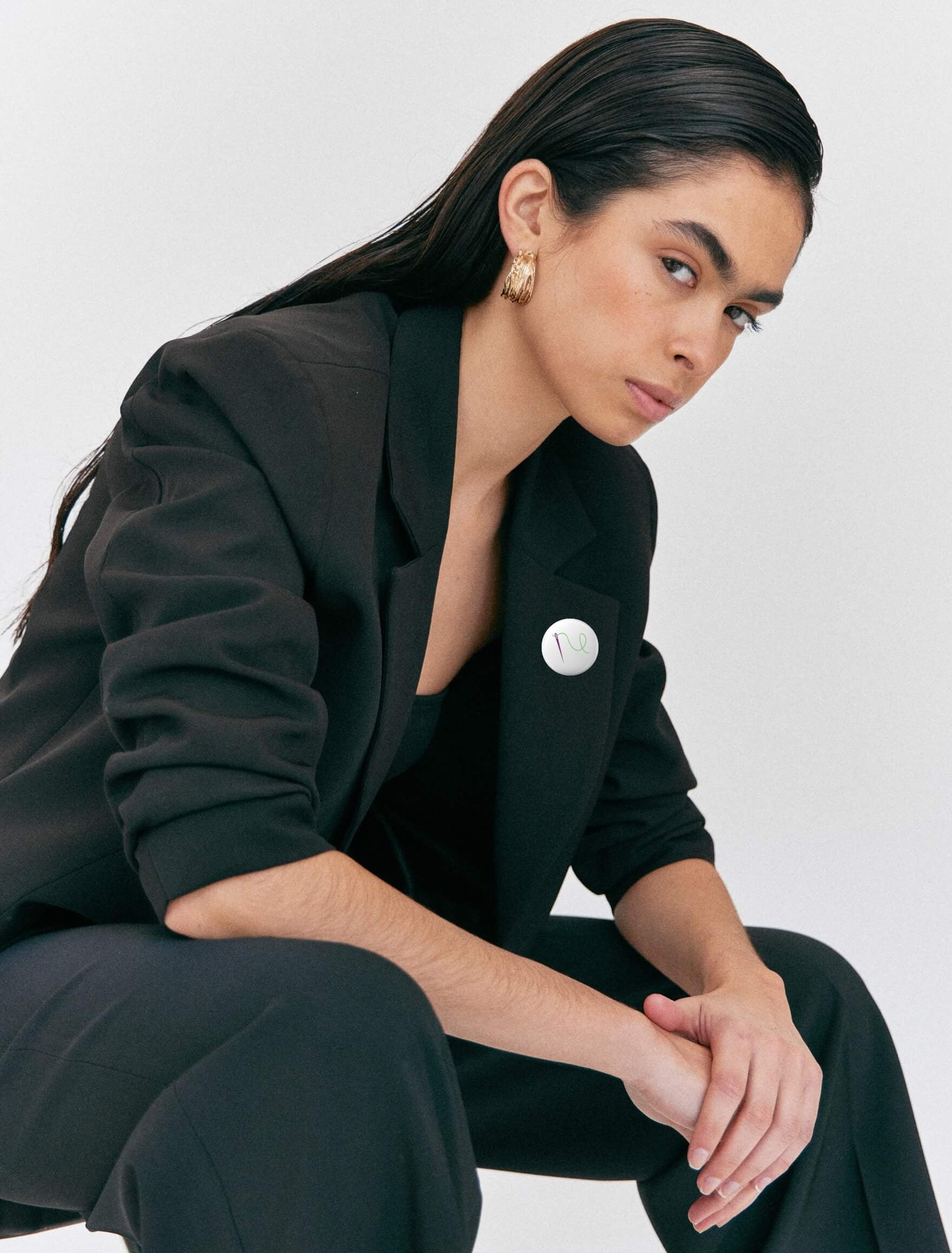 Serious woman in black suit wearing Feminist Threads logo suffragette pin badge – minimalist feminist fashion statement